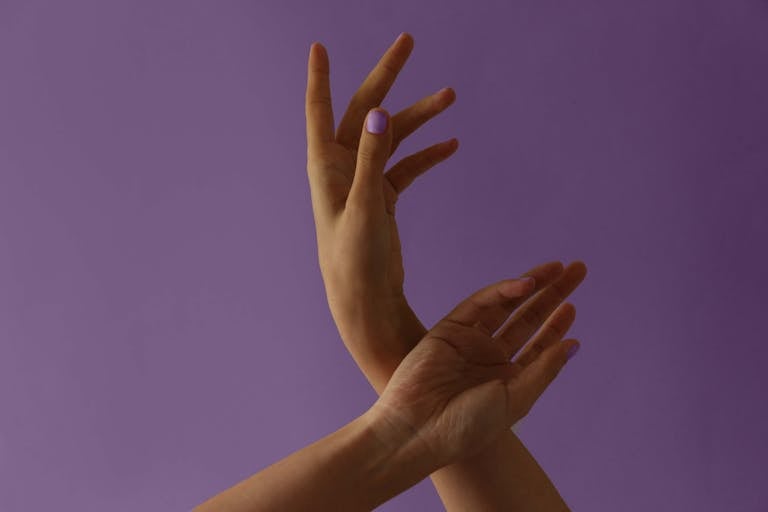 Artistic close-up of graceful hands against a purple backdrop, conveying expression and style.