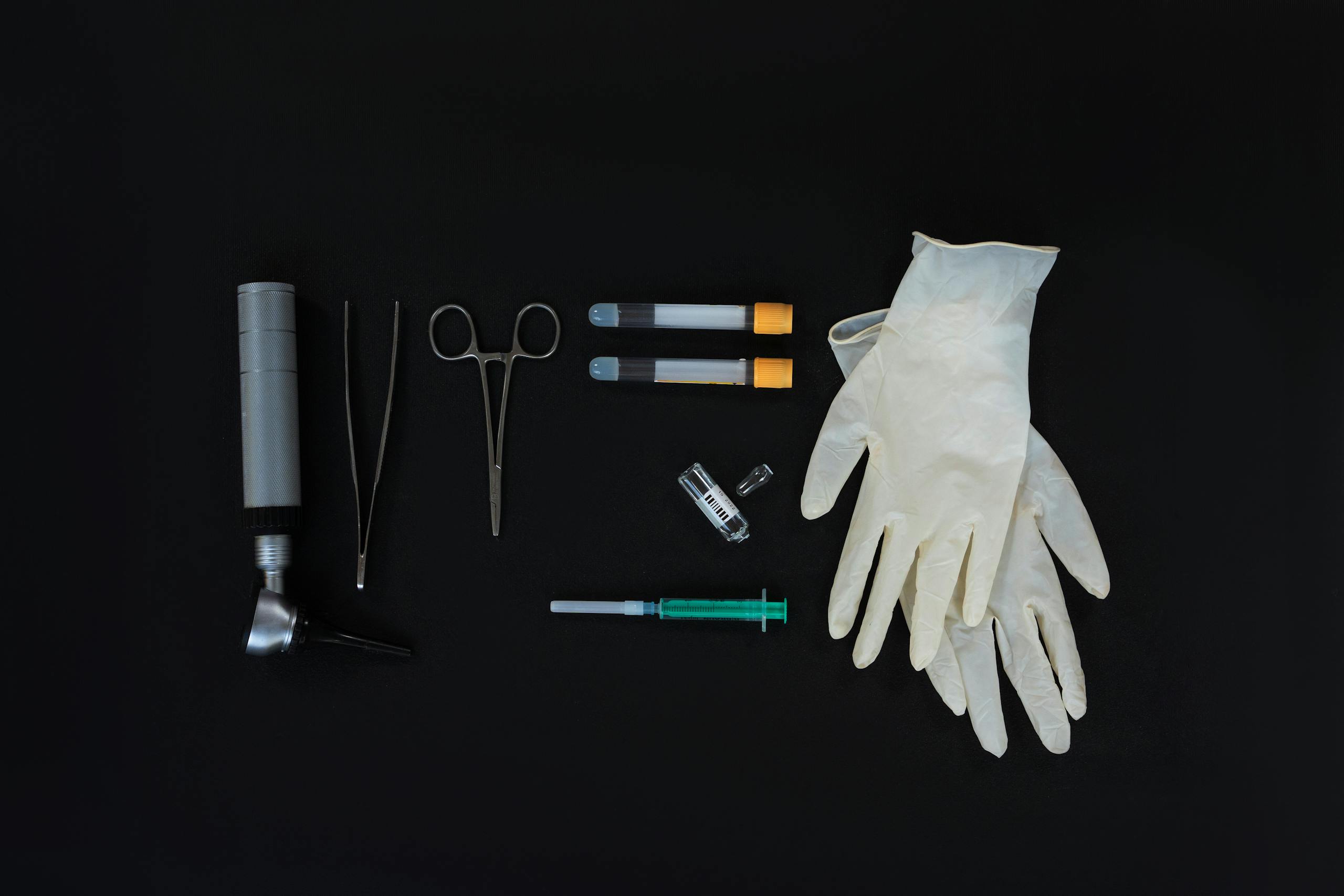 Flat lay of essential medical tools on a black background, including gloves and syringe.